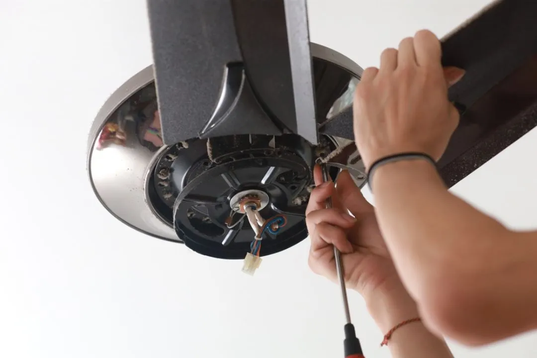 Electrician using screwdriver to install ceiling fan motor and blades, demonstrating professional ceiling fan installation on the Sunshine Coast.