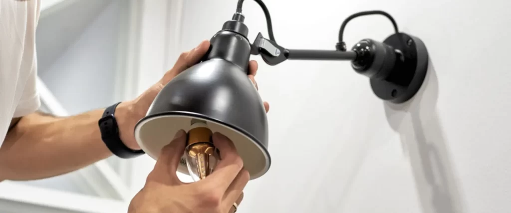 Electrician installing a vintage-style LED light bulb in a black wall-mounted lamp, demonstrating professional residential electrical services on the Sunshine Coast.