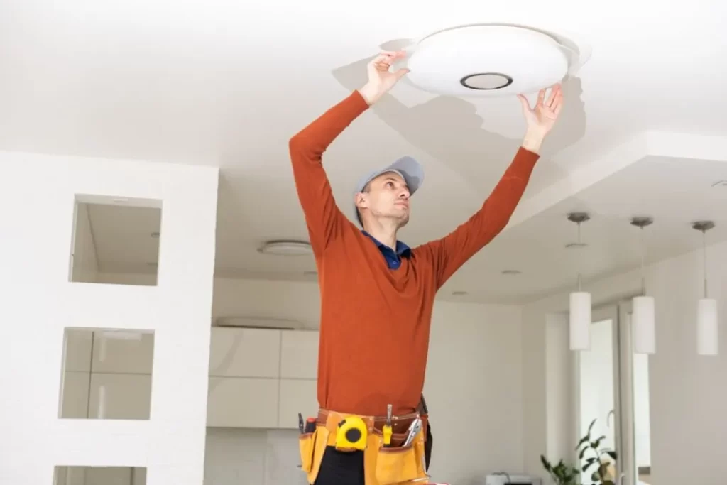 Electrician installing ceiling light fixture in modern home, demonstrating professional residential electrical services on the Sunshine Coast.