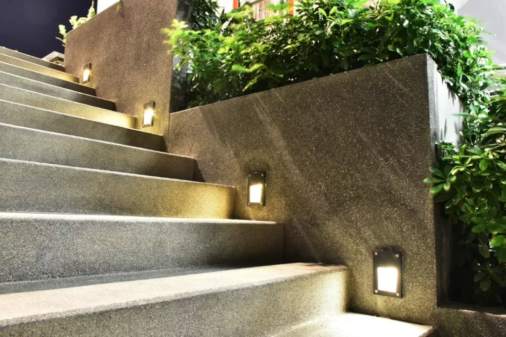 Outdoor concrete staircase with built-in LED step lights and surrounding greenery at night.