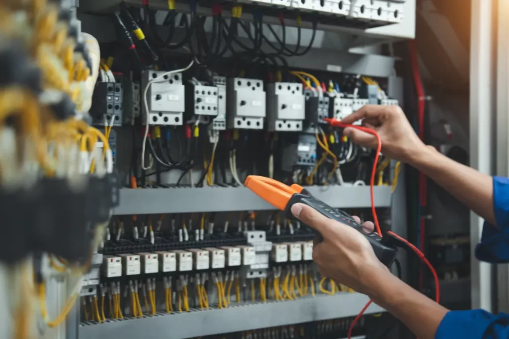 Electrician using a clamp meter to test current in electrical switchboard wiring