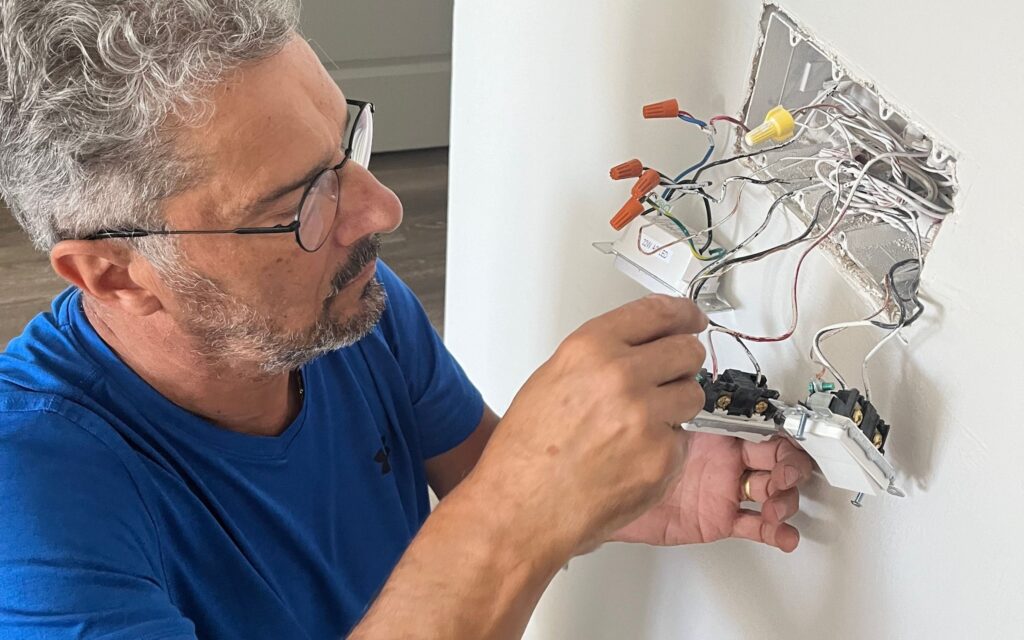Experienced electrician from Sunshine Coast Electrician repairing and wiring a wall switch with multiple electrical wires