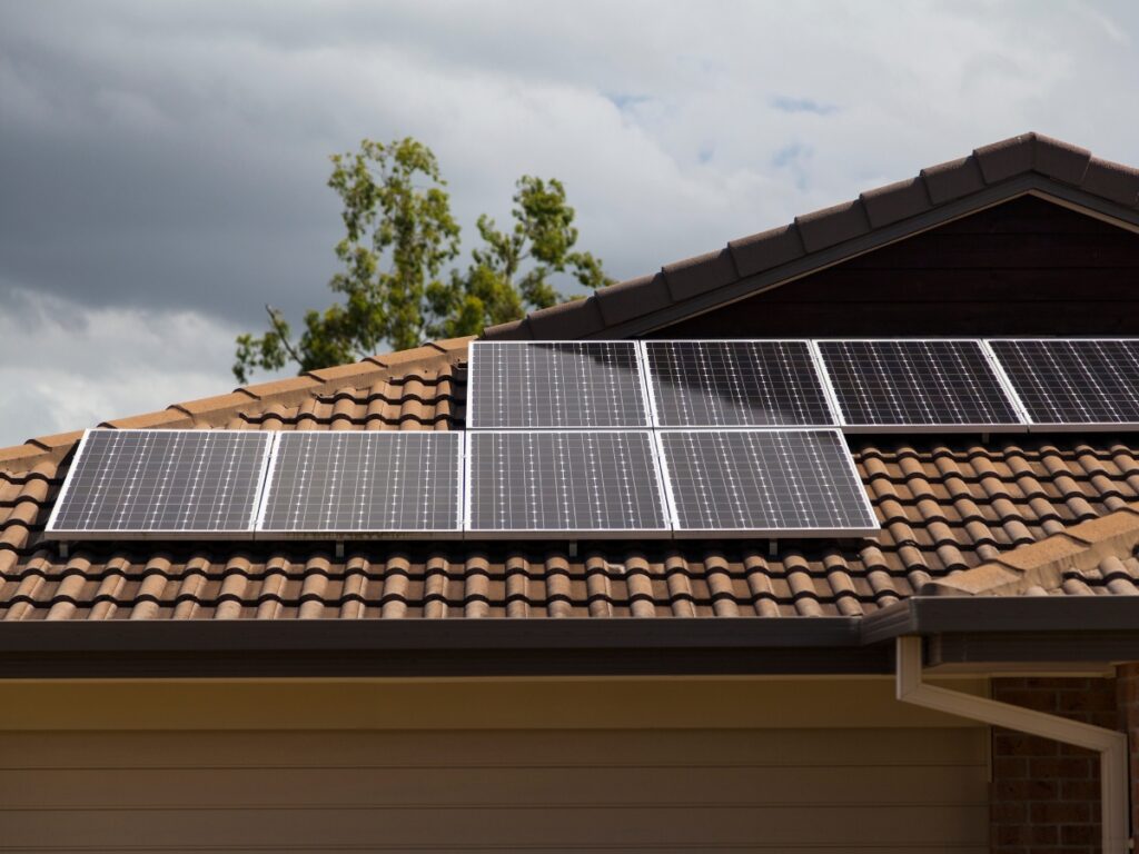 Homeowner viewing solar rebate incentive information on a smartphone with solar panels in the background, representing Queensland's solar rebate program.