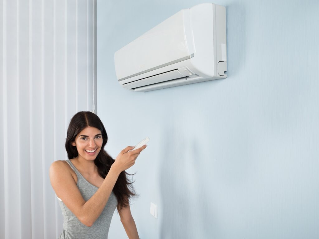 Woman relaxing on a sofa adjusting an energy-efficient air conditioning unit with a remote in a modern Sunshine Coast home.